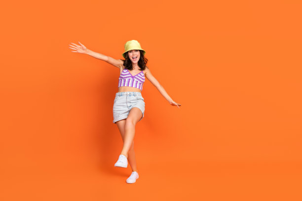 穿着紫色泳衣的迷人甜美女性在橙色背景下的空旷空间中快乐地行走的全身照片图片下载