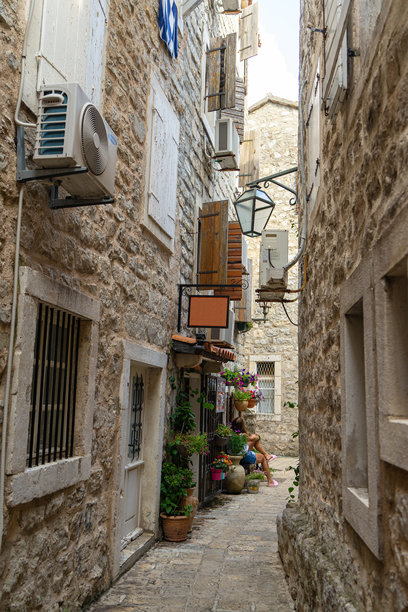 女孩坐在科托尔市狭窄的街道上，周围是花盆，黑山。中世纪小镇位于亚得里亚海的科托尔湾岸边。竖版图片图片下载