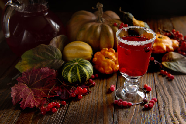 饮用蔓越莓汁、浆果热红酒以及秋天的落叶和南瓜。低调的暗色照片，背景为深色木材。图片下载