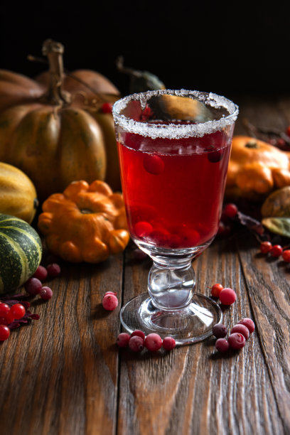 饮用蔓越莓汁、浆果热红酒以及秋天的落叶和南瓜。低调的暗色照片，背景为深色木材。图片下载