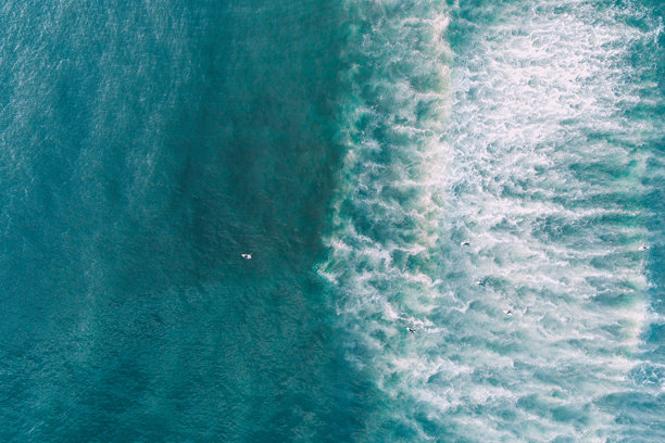 日出时分，海滩岸边的波浪景观，以及冲浪的人们。无人机拍摄的俯视照片。图片下载
