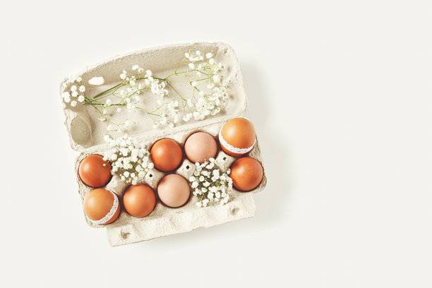 棕色复活节彩蛋装饰着蕾丝和白色满天星花，放在纸箱中，背景为白色。复活节庆祝概念。复古色调的彩绘鸡蛋节日美食俯视照片。图片下载