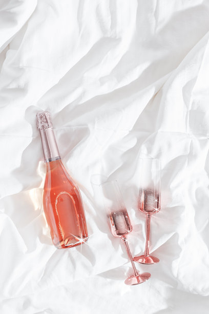 闪亮的香槟杯和一瓶气泡玫瑰酒放在床单上。极简生活美学照片，情人节，浪漫与爱情概念，浪漫约会，夜晚休息，俯视图。图片下载