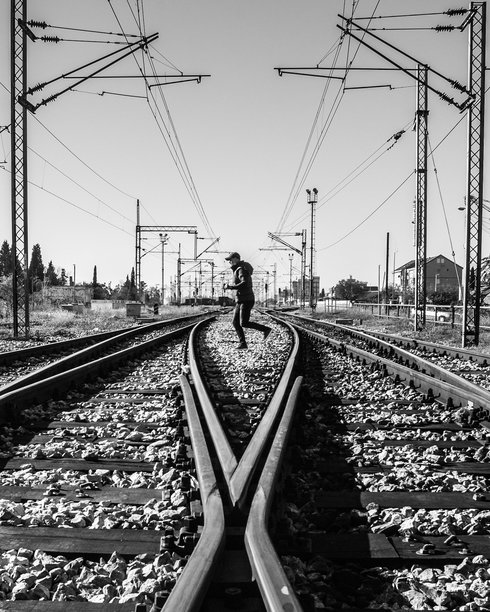 黑白照片中，一个人在开阔天空下走在铁路轨道上图片下载