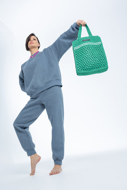 美丽的模特外貌女性。女孩穿着灰色卫衣，手提绿色包，背景为浅色。时尚妆容的漂亮女性在摄影棚中摆姿势。竖版照片。图片下载