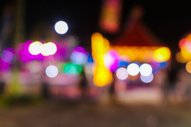 夜市美食摊位的模糊图像，背景为色彩斑斓的夜晚灯光和虚化效果。夜间节日城市公园的抽象照片，模糊的人群与灯光交织。图片下载