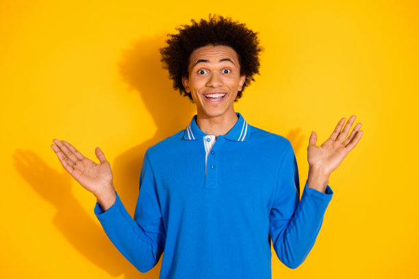 时尚蓝色服装的帅气年轻男士在黄色背景下兴奋地举起双手的照片肖像图片下载