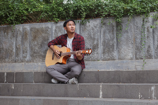 早晨在城市公园里弹吉他的迷人亚洲男子的户外照片图片下载