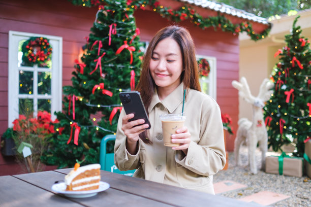 圣诞派对上，一位女性手持手机和一杯咖啡，桌上还有一块蛋糕的肖像照片图片下载