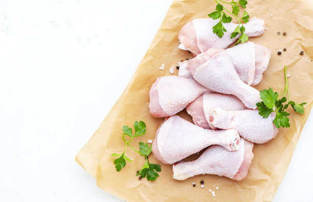 生鸡腿放在羊皮纸上，撒有胡椒、盐和香 parsley。白色背景，俯视图。适合烹饪博客、肉店和在线商店配送的现成图片。图片下载