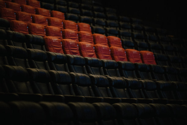 一张空荡荡的电影院照片，红色和黑色的座椅排成行，延伸入黑暗中。图片下载