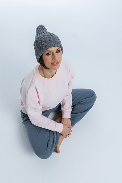 穿着灰色帽子的美丽女性肖像。女孩坐在地板上，双腿交叉。工作室摄影。竖版照片。图片下载