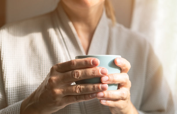 的白人女性在家中窗边喝茶或咖啡。家庭生活方式的概念。阳光明媚的日子里，穿着浴袍的现代快乐中年女士的特写照片。图片下载