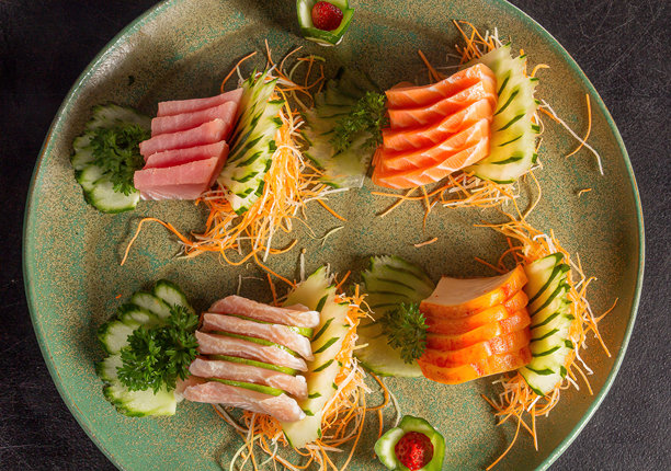 各种日本食品鱼类的切片，如寿司和生鱼片，以及各种蔬菜，摆放在黑色桌子上的绿色复古盘子里，特写照片展示了质感。图片下载