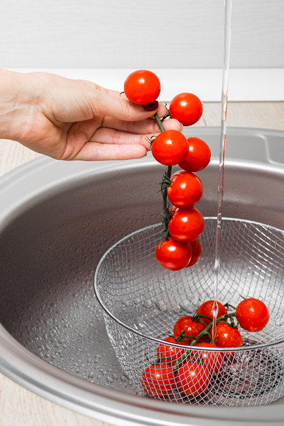女人在厨房水槽中清洗樱桃番茄，竖版照片图片下载