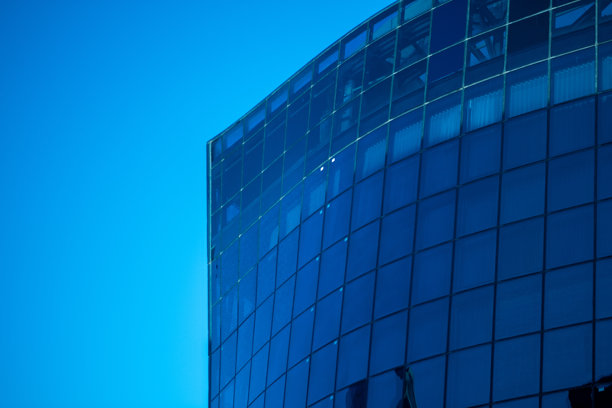 现代弯曲玻璃建筑顶部细节，商业企业背景，建筑物映衬在蓝天之下，4K库存照片图片下载