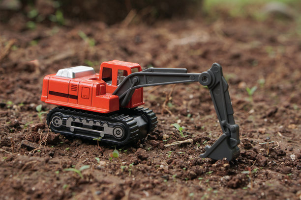 橙色挖掘机玩具从侧面视角在户外土壤上挖掘。挖掘机模型的照片，建筑概念。图片下载