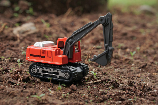 橙色挖掘机玩具从侧面视角在户外土壤上挖掘。挖掘机模型的照片，建筑概念。图片下载
