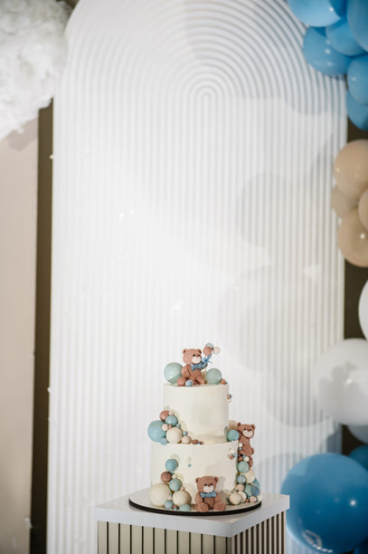 美味的接待。时尚的生日蛋糕，上面有小熊造型，适合1、2、3岁的小男孩特写。照片墙装饰有棕色、蓝色和金色气球。庆祝洗礼的概念。生日派对。图片下载