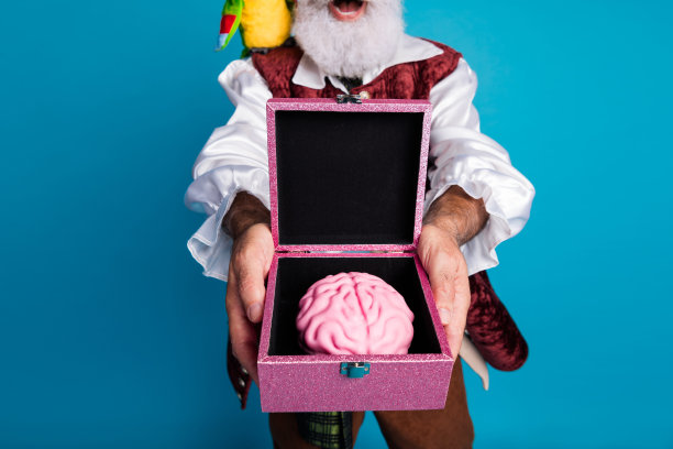 穿着狂欢派对服装的老搞笑海盗男性，手持脑箱，背景为蓝色，照片裁剪过。图片下载