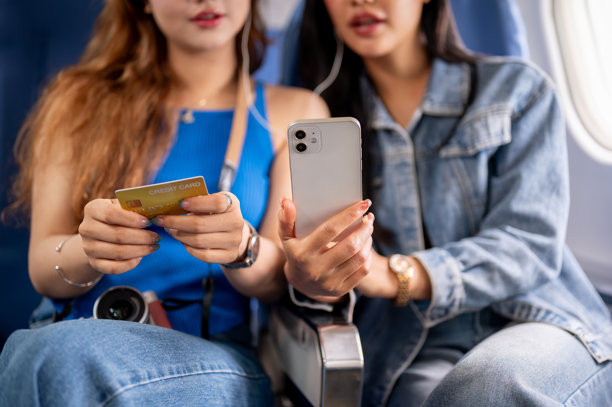 两位亚洲女性朋友一起乘飞机旅行的特写照片，一人手持信用卡。图片下载