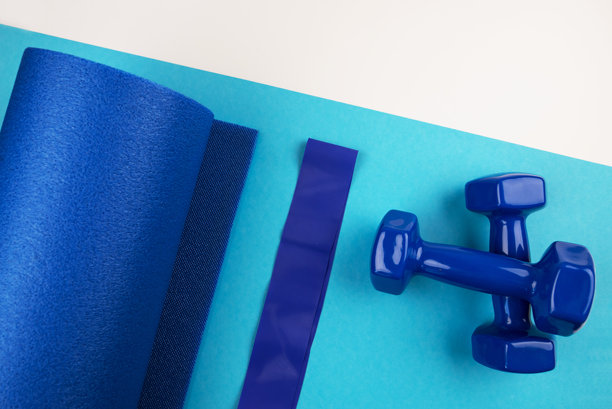 运动配件的概念。蓝色哑铃、蓝色瑜伽垫和其他运动器材的俯视照片，背景为蓝色和白色。图片下载