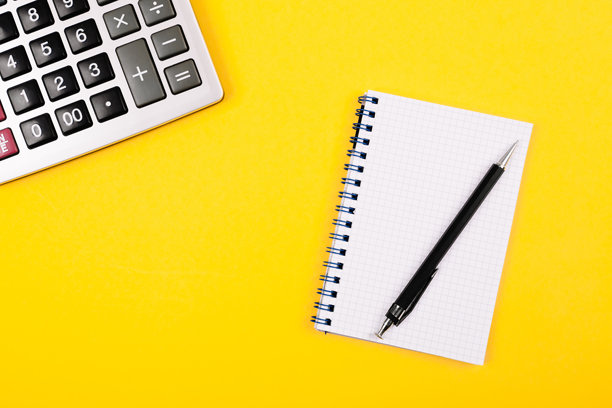 大型银色计算器、黑色钢笔和白色纸质笔记本放在黄色背景上。概念照片，涉及计算、会计、计算、利润、损失和税务。图片下载