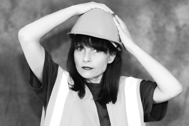 黑白照片：一位长发女性建筑工人正在调整安全头盔图片下载