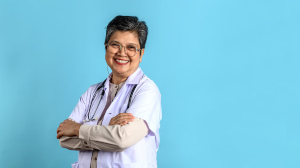 蓝色背景下的老年亚洲女性医生的工作室肖像照片，背景留有空白空间。图片下载