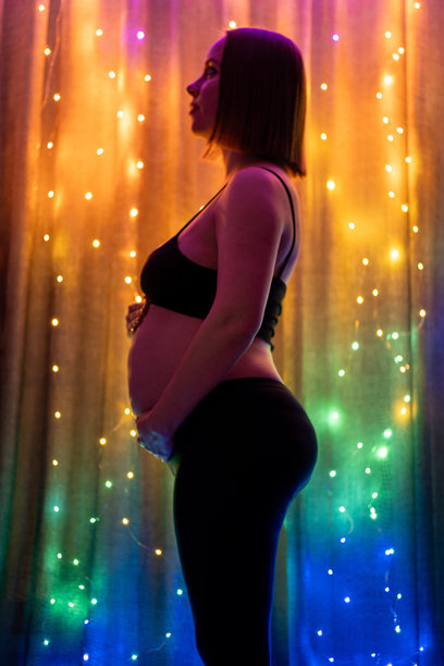 怀孕的女性在闪烁的灯饰旁。孕妇身体轮廓照片。圣诞快乐，新年奇迹。图片下载