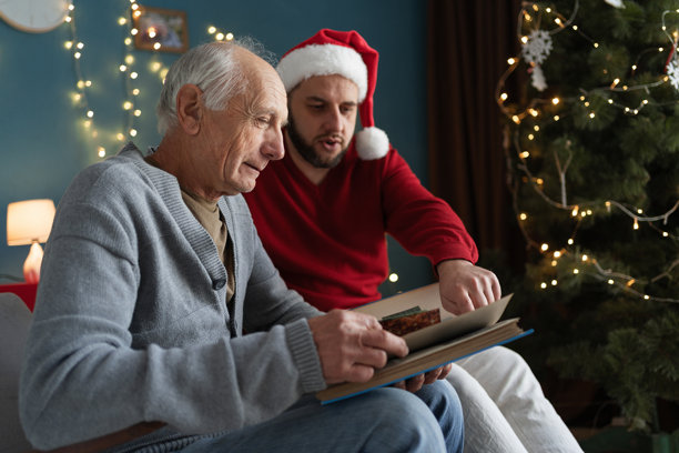 老父亲和成年儿子一起观看相册。家庭传统，圣诞节时查看照片。图片下载