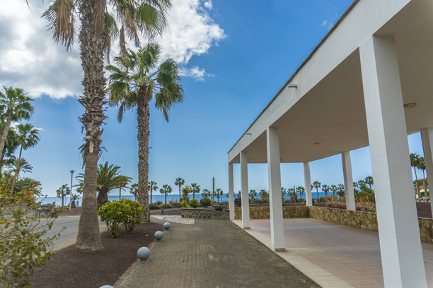 福特文图拉岛格兰塔哈镇的全景。照片展示了沿着沙滩排列的五彩缤纷的建筑，温柔的海浪在晴朗的蓝天下轻轻拍打着海岸。图片下载