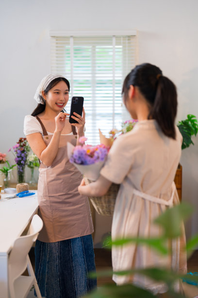 一位花店老板拍摄花束的照片，而另一位花店老板欣赏这件作品，展示了在热闹花店中的团队合作。图片下载