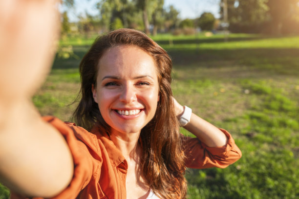 快乐的白人女性在城市公园户外自拍，使用智能手机发送照片信息。图片下载