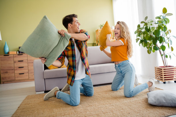 年轻情侣在现代明亮的春季舒适公寓室内进行枕头大战，享受快乐时光的全身照片图片下载