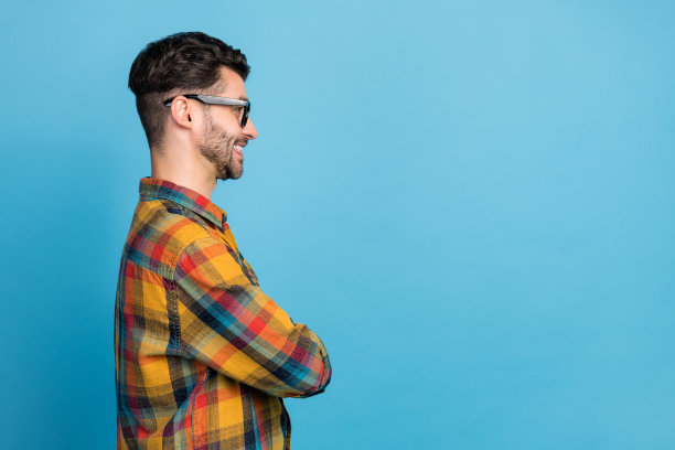 侧面照片，聪明自信的戴眼镜男士，穿着格子衬衫，微笑着看向空旷的空间，背景为蓝色。图片下载