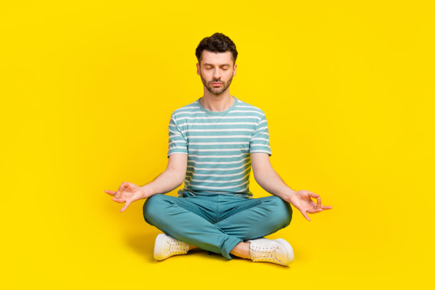 年轻男子穿着蓝色条纹T恤和裤子，在黄色背景下工作后冥想的全身照片图片下载