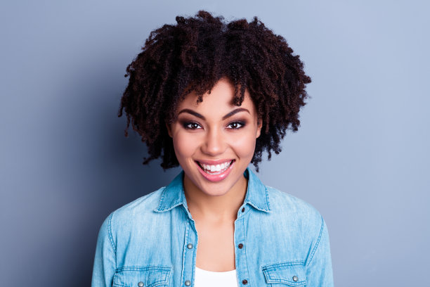 特写照片，展现了一位美丽乐观的女孩，时尚的牛仔风格波浪发型，灿烂的笑容，背景为灰色。图片下载