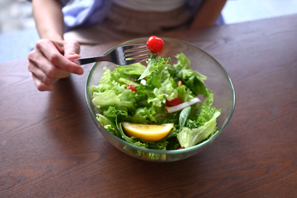 一碗健康新鲜的绿色沙拉，里面有生菜、柠檬、樱桃番茄、胡萝卜和洋葱，摆放在桌子上。库存照片图片下载