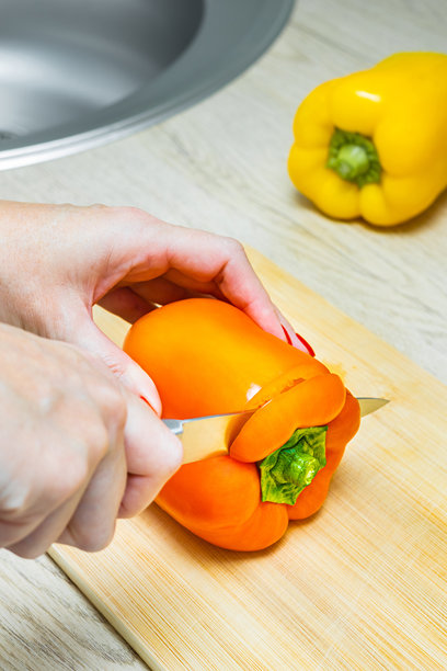 女人在厨房砧板上用刀切青椒，竖版照片图片下载