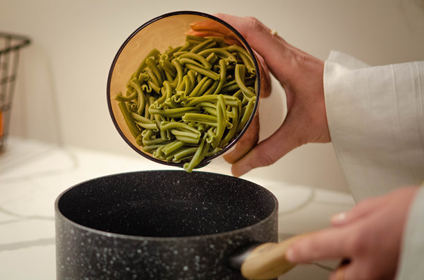 一位年轻女性将新鲜自制的有机绿色意大利面倒入一锅沸水中 - 库存照片图片下载