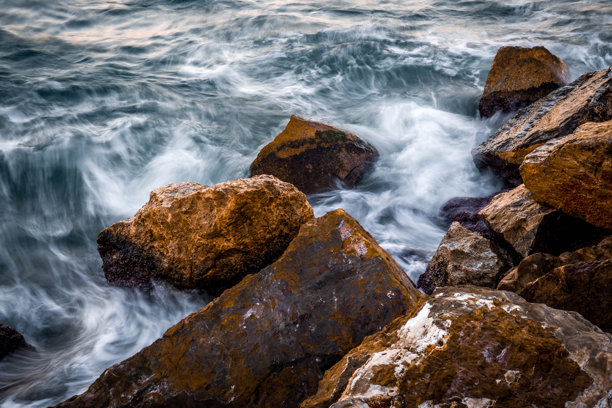 海岸上的石头特写，夕阳下海面呈现丝滑效果。低快门速度拍摄的照片。图片下载