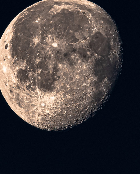 一张近距离拍摄的地球月球照片，显示出可见的陨石坑和不同的色调与阴影，背景为黑色天空。图片下载