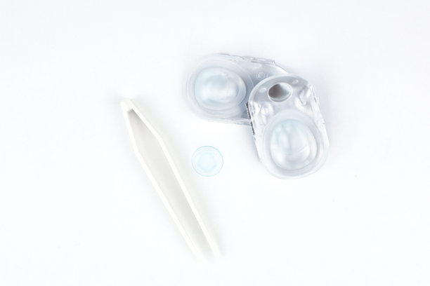 两只一次性隐形眼镜容器和一只蓝色软镜片以及米色镊子位于照片中央，背景为白色，特写并留有文本空间。眼科、视力、视力矫正的概念。图片下载