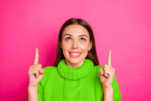 特写照片，快乐的女孩穿着黄色毛衣，指向空白处展示广告，背景为鲜艳的紫红色。图片下载