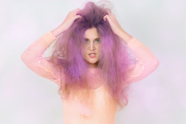 一位紫发女性穿着粉色衬衫。她的发型有些凌乱，面带皱眉看向镜头。整张图片散发出一种略显叛逆和前卫的氛围。图片下载