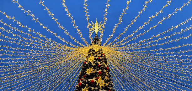 户外的圣诞树，装饰着灯光、星星和花环，背景是蓝天 - 横向照片图片下载