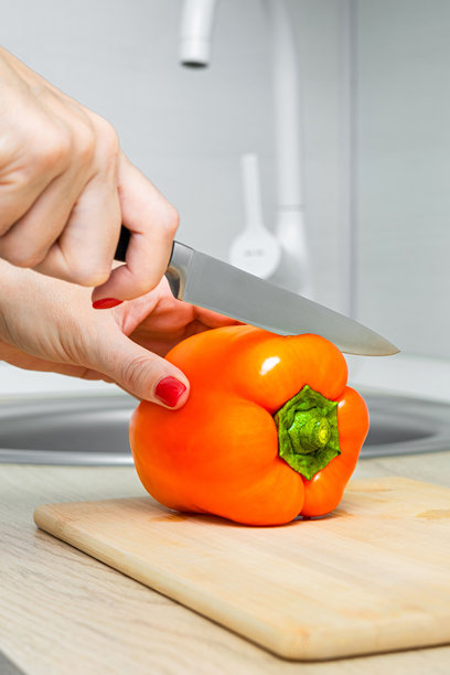 女人在厨房砧板上用刀切青椒，竖版照片。图片下载