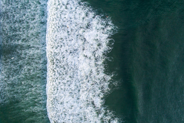 日出时分，海滩岸边的波浪景观，以及冲浪的人们。无人机拍摄的俯视照片。图片下载
