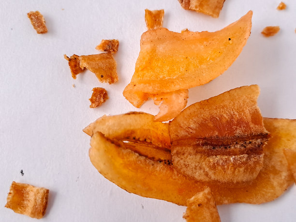 三片干香蕉片的照片，背景为纯白色。这些香蕉片呈现出丰富的金橙色，表面有干燥过程留下的明显纹理。香蕉中的天然糖分已经焦糖化。图片下载